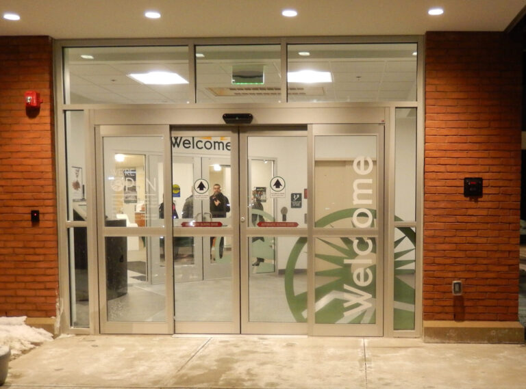 New England Federal Credit Union Glass entrance doors to a building with "Welcome" written on them; people and interior visible through the glass.