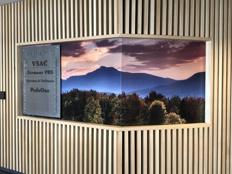 VSAC Digital Printed Wall A wall display with a sign listing businesses and a large landscape photo of mountains and trees at sunset.