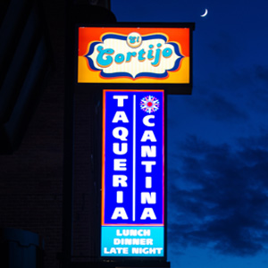Electric El Cortijo Neon sign for El Cortijo Taqueria Cantina, advertising lunch, dinner, and late night against a dark sky.