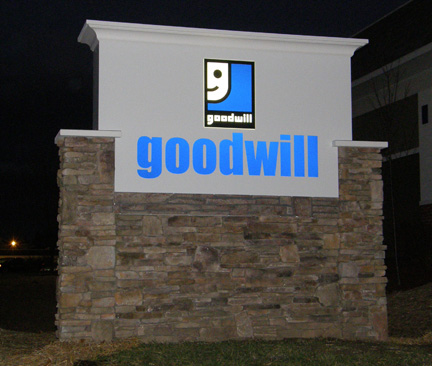 Goodwill Sign Illuminated Goodwill sign with logo on a stone base, photographed at night outside a building.