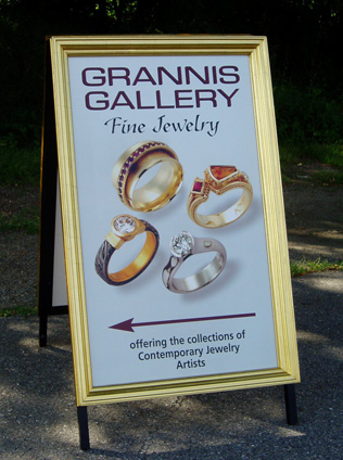 Grannis Gallery A sign advertising Grannis Gallery Fine Jewelry, featuring images of four rings and information about contemporary jewelry artists.