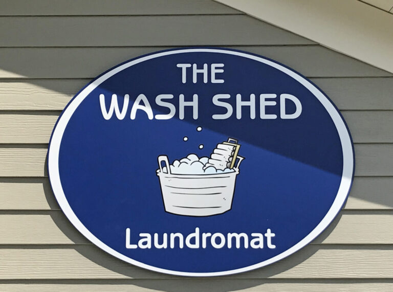 PVC Sign with High Performance Digitally Printed Blue and white sign reading "The Wash Shed Laundromat" with an illustration of a bucket filled with soapy laundry.