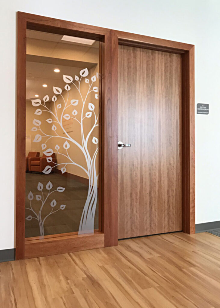 Wooden door with a glass panel on the left, decorated with a white tree and leaf design. Light wood floor.