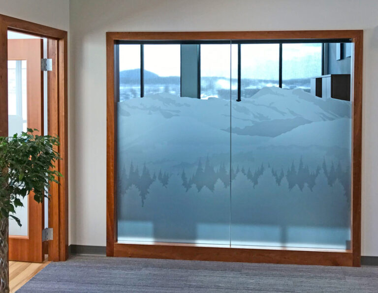 Digital Printed Etched Vinyl Glass wall with frosted mountain and tree design, framed in wood, next to a doorway and a potted plant.