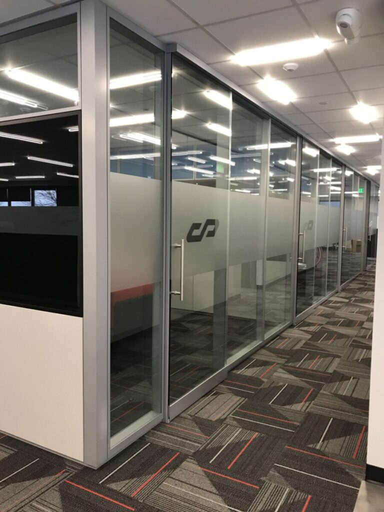 Custom Etched Vinyl A glass-walled office hallway with patterned carpet, frosted glass panels, and overhead fluorescent lighting.