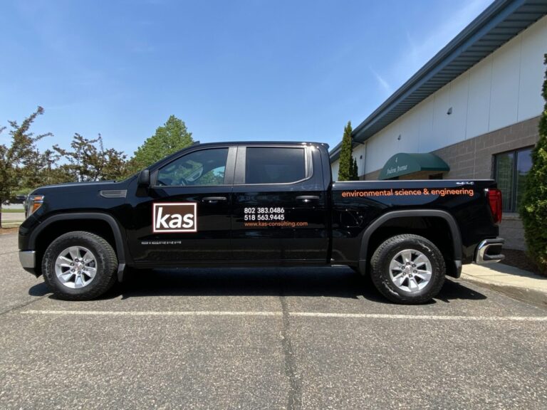 KAS Vinyl Lettering A black pickup truck with KAS branding and contact info, parked outside a building on a clear day.