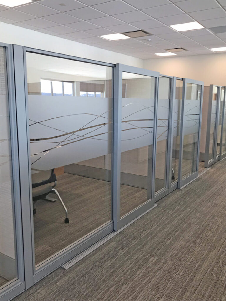 Custom Etched Vinyl Row of glass office cubicles with frosted designs, each containing an office chair, in a carpeted workspace.