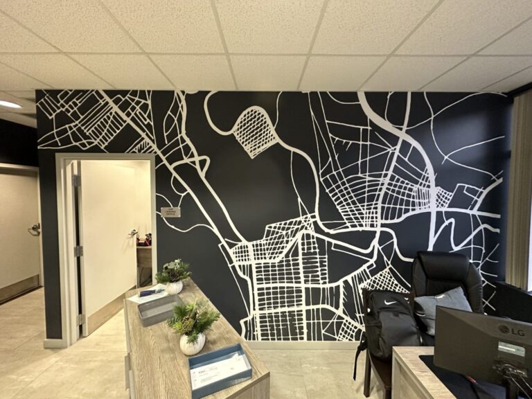 White Vinyl Graphic Office interior with a black-and-white abstract map mural on the wall behind a desk, plants, and office supplies.