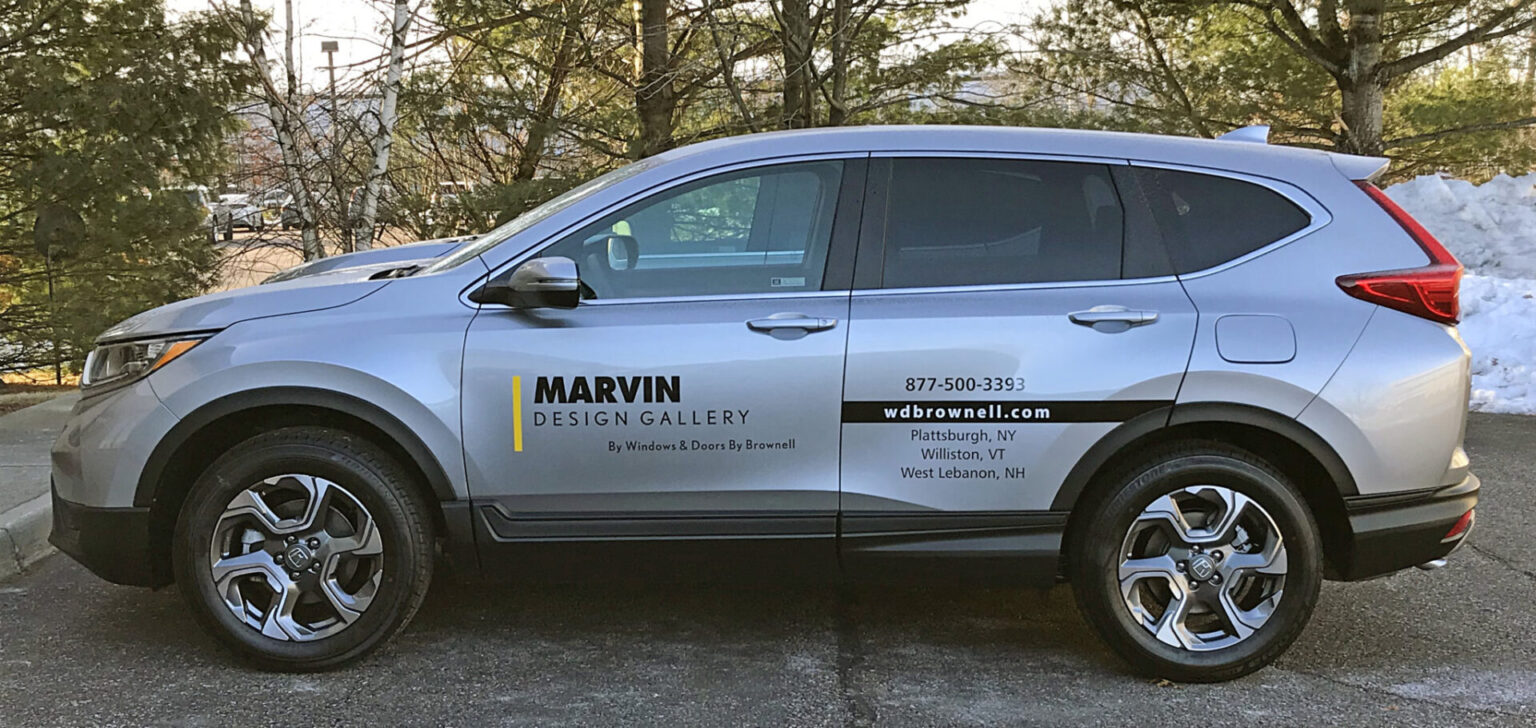 Marvin Design Vinyl Lettering Silver SUV with "Marvin Design Gallery" branding and contact info parked outdoors near trees and snow.