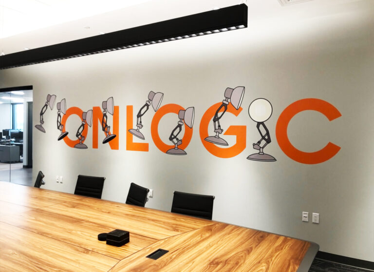 Onlogic Vinyl Wall Graphic Conference room wall with "ONLOGIC" in orange, some letters formed by animated desk lamps; wood table in foreground.