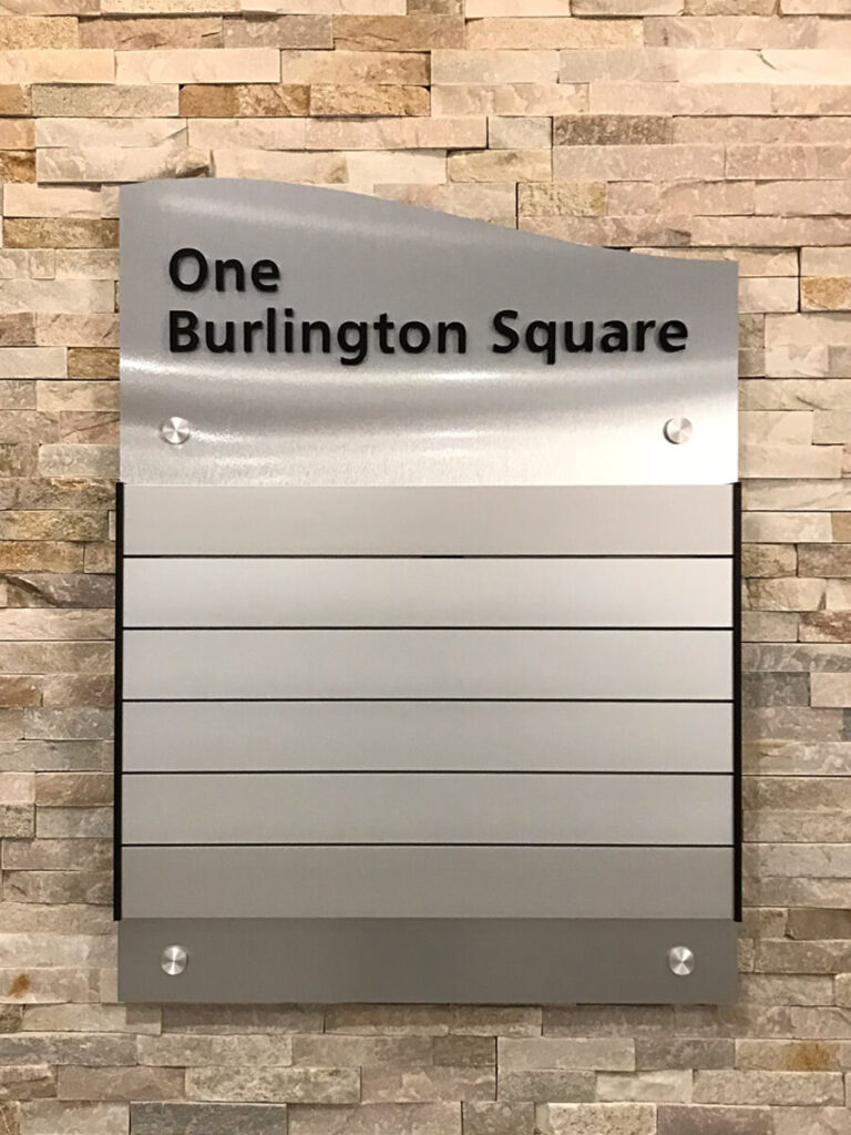 Burlington Square Directory Metal directory sign reading "One Burlington Square" with empty name slots, mounted on a stone wall.