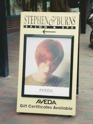 Stephen & Burns A sidewalk sign for Stephen & Burns Salon & Spa with a photo of a model and text about Aveda gift certificates.