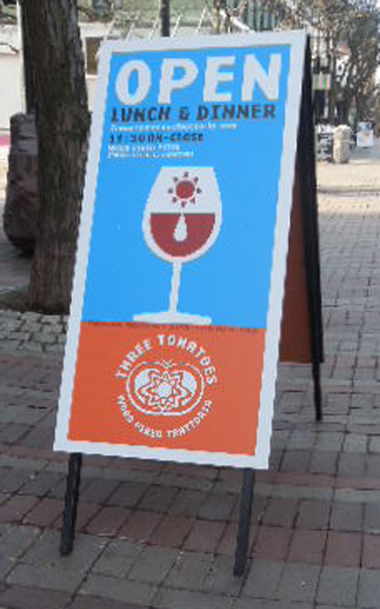 Three Tomatoes Sidewalk Frame A sidewalk sign reads "OPEN LUNCH & DINNER" with a wine glass graphic and "Three Tomatoes" restaurant logo below.