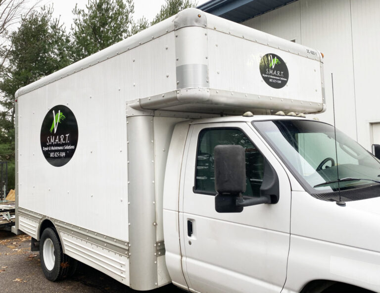 V Smart Vinyl Logo White box truck with "S.M.A.R.T. Repair & Maintenance Solutions" logo parked beside a light-colored building.