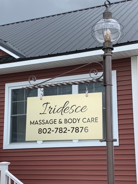 Iridesce Massage A sign for Iridesce Massage & Body Care with a phone number, displayed outside a red building near a window and lamp post.
